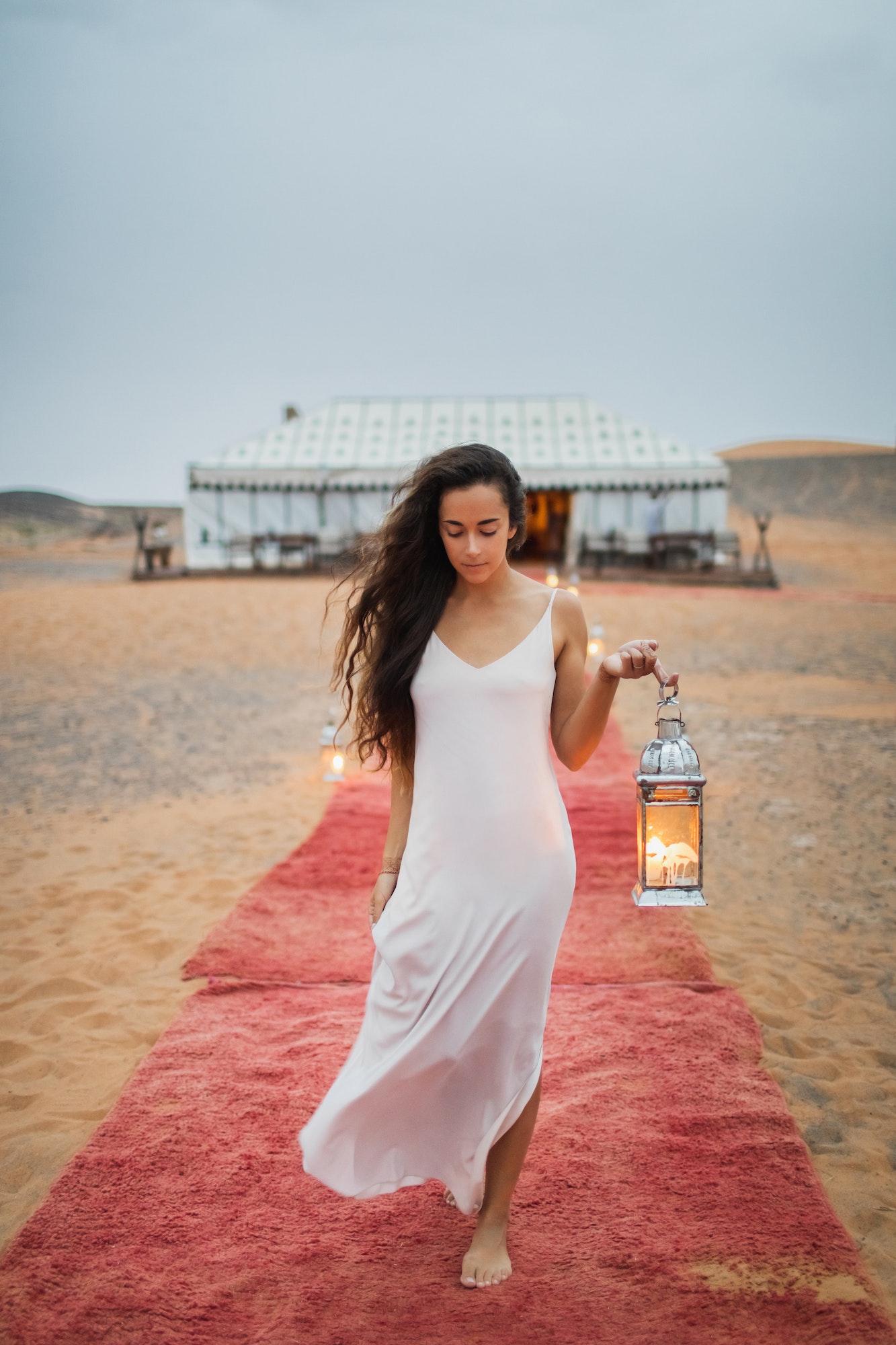 Beautiful oriental young brunette woman in white dress walking near luxury glamping tent camp