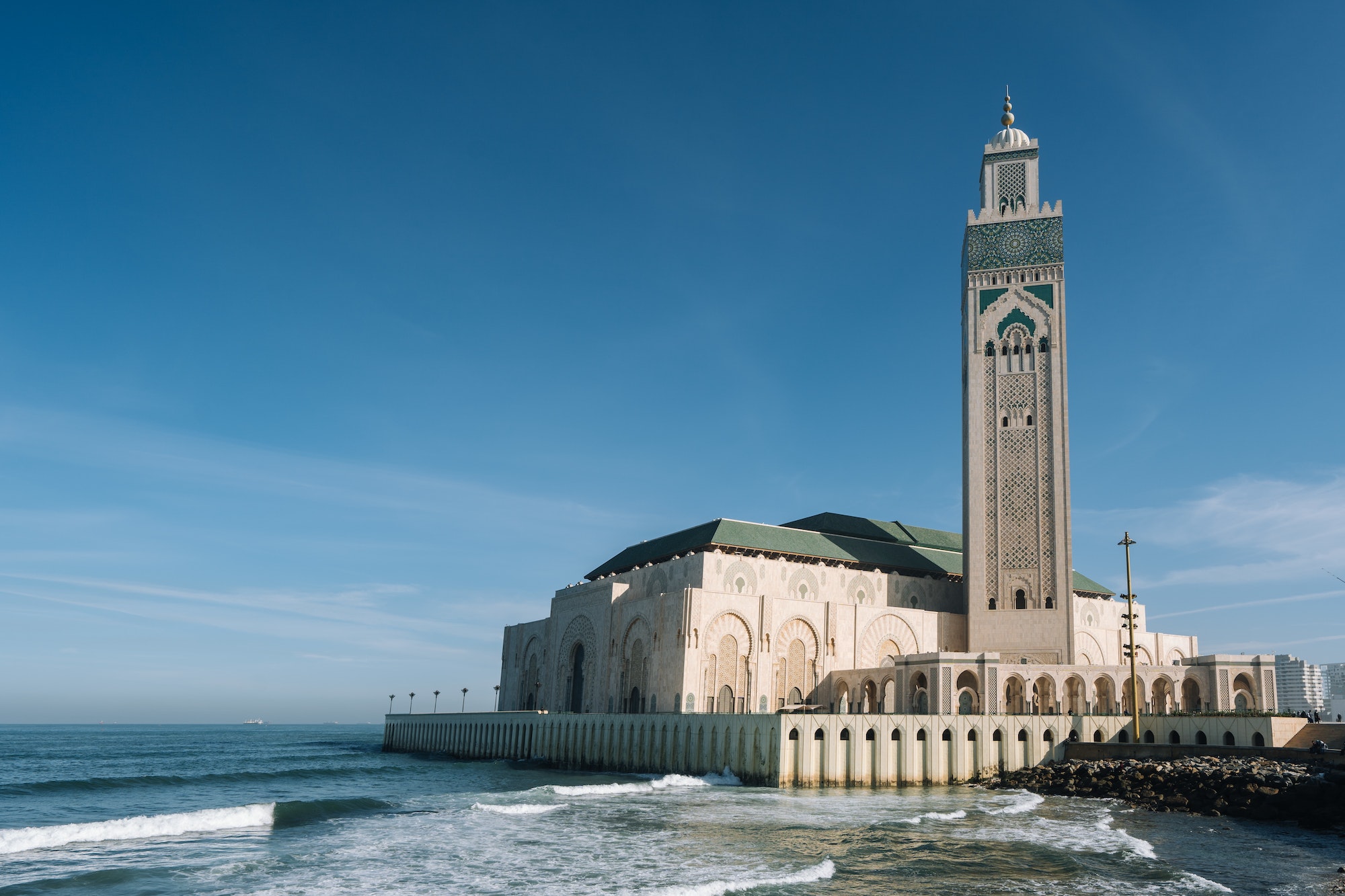 Hassan II Mosque surrounded by water and buildings under a blue sky and sunlight