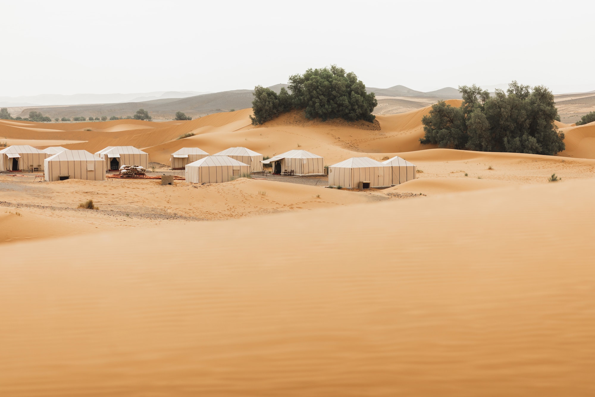 Luxury glamping camp in Morocco Sahara desert. Sand dunes around. Many white modern eco tents.