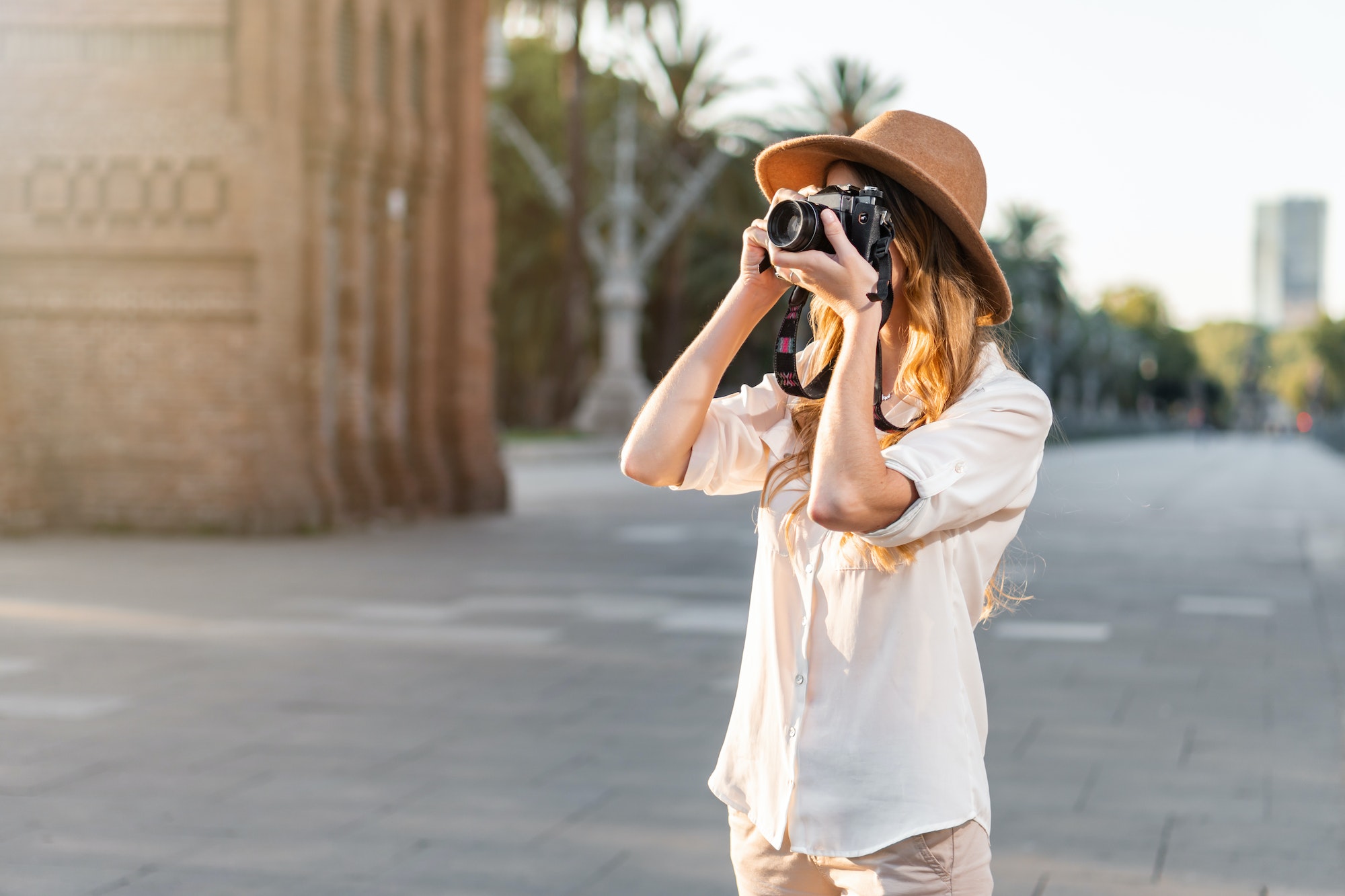 Shallow focus of a young female tourist with a fedora hat photographing in Barcelona, Spain