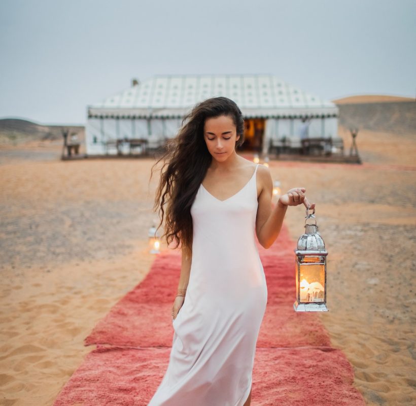 Beautiful oriental young brunette woman in white dress walking near luxury glamping tent camp