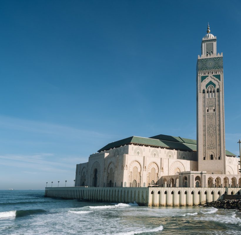 Hassan II Mosque surrounded by water and buildings under a blue sky and sunlight