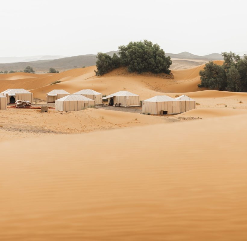 Luxury glamping camp in Morocco Sahara desert. Sand dunes around. Many white modern eco tents.