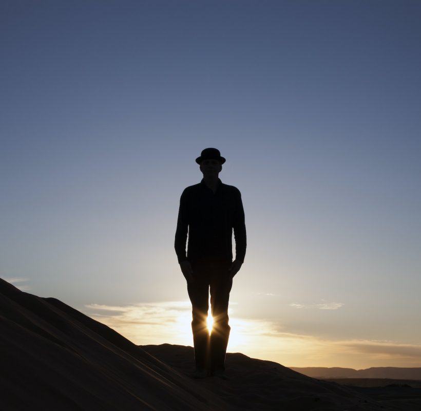 Morocco, Merzouga, Erg Chebbi, silhouette of man wearing a bowler hat standing on desert dune at sun, 9 days to Desert from casablanca