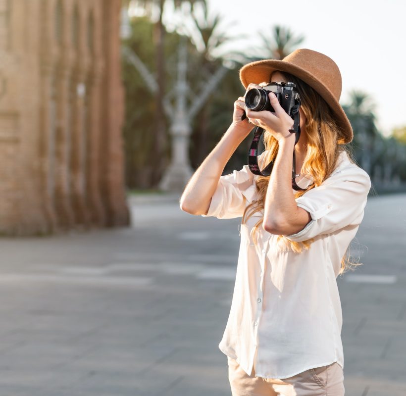 Shallow focus of a young female tourist with a fedora hat photographing in Barcelona, Spain