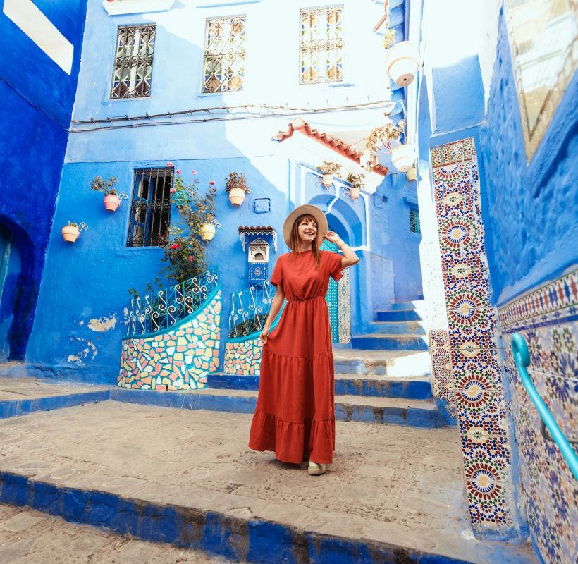 Young woman with red dress visiting the blue city Chefchaouen, Marocco